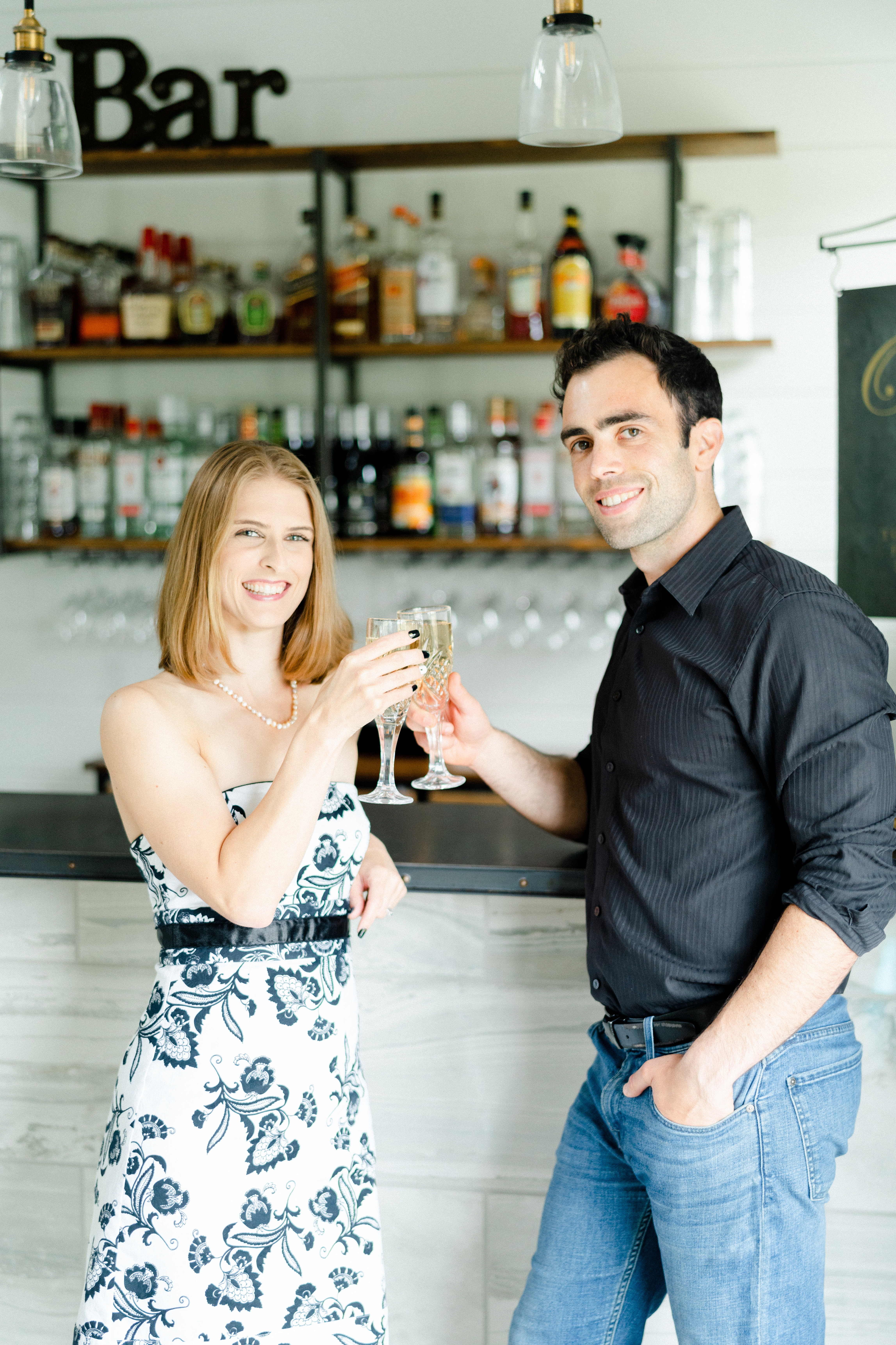 Two people clinking champagne glasses behind a bar at a wedding venue, representing the founders of Elevated Venue Management.